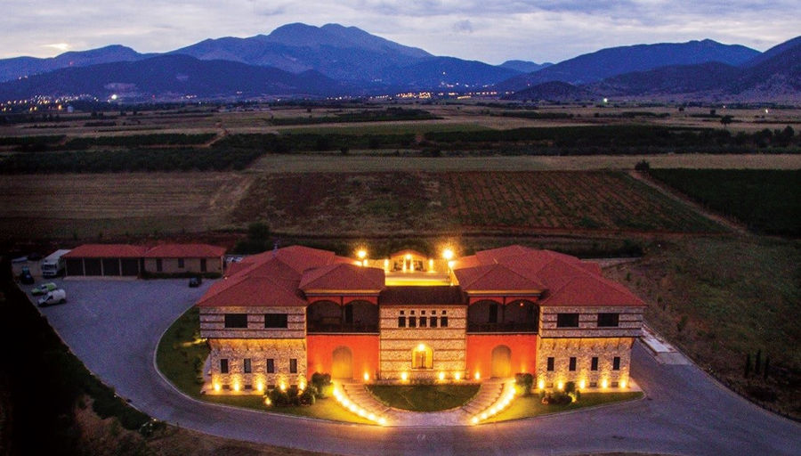illuminated 'Oenogenesis Estate' frome above by night surrounded by pavement and trees and vineyards